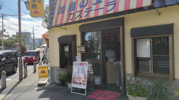 加島の卵焼きの店舗を斜め右から撮影・クリーム色の建物に、白とオレンジのストライプの屋根に「加島の卵焼き カステーラ」という文字が書かれています