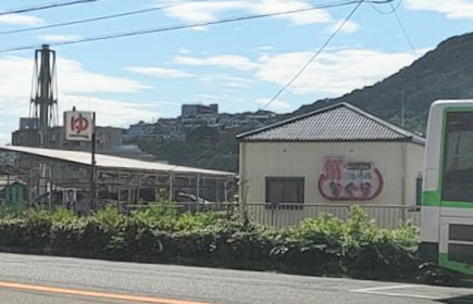 名倉にある「ゆうぇ〜ぶ・なぐら」という銭湯の写真です。道路脇にあり、背後には山が見えます。