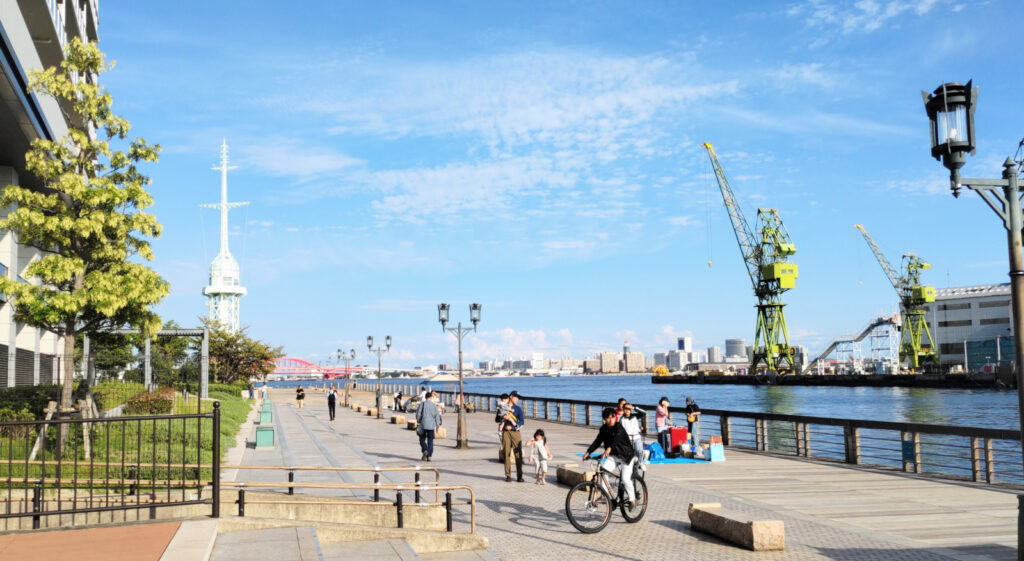 青空の下に海が広がっている広場のようなところ。たくさんの人が自転車や徒歩で行き交っています