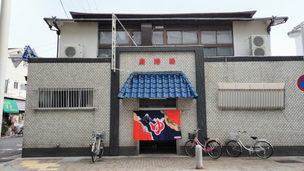 扇港湯の写真です。煉瓦造りの二階建ての建物に、青い瓦屋根のひさし。ひさしの下に「ゆ」と書いた暖簾がたなびいています。