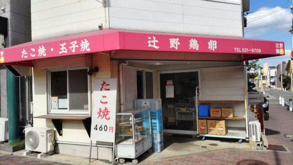 国道25号線沿いにある「辻野鶏卵」というお店。赤い屋根に「たこ焼・卵焼　辻野鶏卵」と書かれています。白い看板に赤い文字で「たこ焼　460円」と大きな文字で書かれた看板も出ています。その背後には卵焼の見本が飾ってあるショーケースが置かれています。